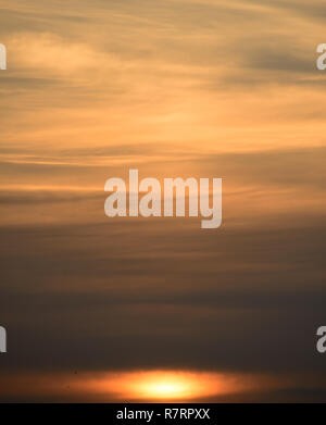 Low undefined Sun and muted soft pastel yellow orange clouds at sunset .Dramatic sky. Stock Photo