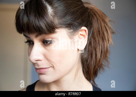 Young woman three quarters  close-up portrait. Caucasian with brown long hair  in ponytailand bangs. Smiling expression, looking down. Stock Photo