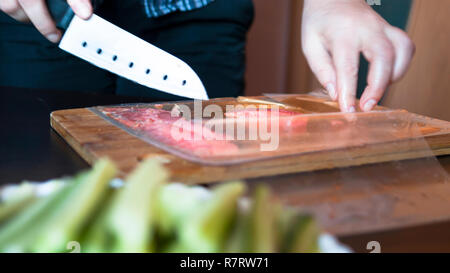 Woman Is Cutting Red Fish, Trout Fillet Packaged In Plastic Vacuum Pack On A Wooden Board.  Hands Hold A Santoku Knife With Holes.  Blurred Cucumber S Stock Photo