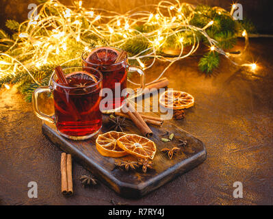 Glass cups of hot mulled wine with spices and dry orange pieces on wooden cutting board on dark background. Traditional Christmas drink Stock Photo