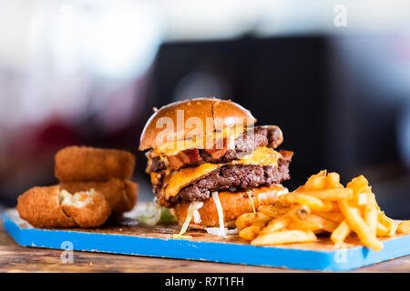 Burger greasy stacked street food, fried french fries closeup, melted cheese and bun on blue tray display in restaurant closeup, breaded fish sticks,  Stock Photo
