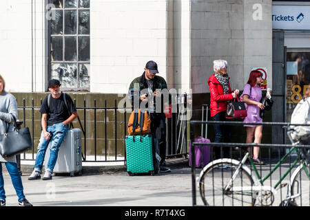London, United Kingdom - September 15, 2018: People standing outside with luggage baggage bags outdoors at building entrance for bus stop buses transp Stock Photo