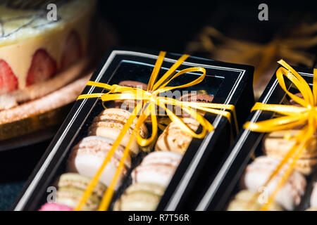 Display of pile of gift box ribbon tied gourmet colorful macaroons macarons on shelf in bakery store shop Stock Photo