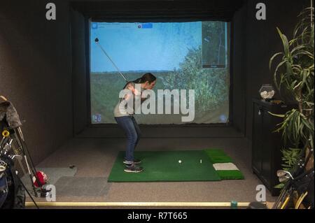 U.S. Air Force Airman 1st Class, Caitlin Oleska, Signals Analyst with the 301st Intelligence Squadron, plays a round of golf on the golf simulator at Arctic Oasis, Mar. 31, 2017, Joint Base Elmendorf-Richardson, Alaska. Due to the accumulation of snow and ice during the winter, the golf season in Anchorage is limited to only 5-6 months. Stock Photo