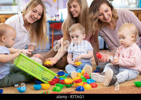 Three woman friends with babies toddlers playing on the floor in sitting room Stock Photo