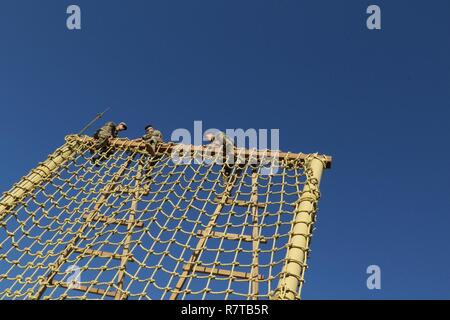 U.S. Servicemembers climb over the top of the ‘Tough One’ obstacle during day zero of U.S. Army Central’s first Air Assault Course, April 4, 2017, at Camp Buehring, Kuwait. The ‘Tough One’ obstacle includes rope, net climbing and walking along wooden planks. It is one of two obstacles candidates must pass in order to continue forward on day zero. The Air Assault Course allows U.S. military personnel in the USARCENT theater of operations the unique opportunity to become air assault qualified, while deployed outside the continental United States. Stock Photo