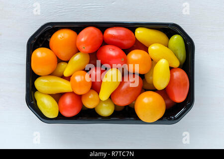 Black tray of fresh homegrown tomatoes of different colors, viewed from above on white wooden background Stock Photo