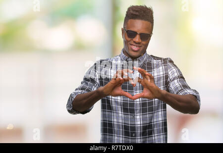 Young african american man wearing sunglasses over isolated background smiling in love showing heart symbol and shape with hands. Romantic concept. Stock Photo