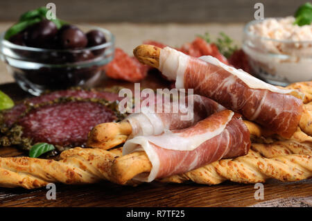 Dish for Antipasto snacks with salami, bread sticks (Grissini) wrapped with prosciutto olives and cheese paste on the wooden surface Stock Photo