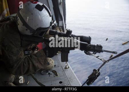 Staff Sgt. Matt Tippett, a chief scout Sniper, Battalion Landing Team, 2nd Battalion, 5th Marines, 31st Marine Expeditionary Unit, fires an M27 Infantry Automatic Rifle in an MH-60S Sea Hawk, over the Pacific Ocean, March 28, 2017. Scout snipers conducted aerial sniper training as part of the 31st MEU’s 17.1 Spring Patrol. As the Marine Corps’ only continuously forward deployed unit, the 31st MEU’s air-ground-logistics team provides a flexible force, ready to perform a wide range of military operations, from limited contingency to humanitarian assistance operations, throughout the Indo-Asia-Pa Stock Photo