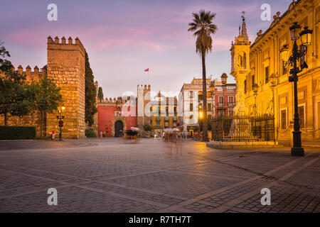 The Plaza del Triunfo in Sevilla, Andalusia, Spain. Shot during twilight. Two blurred horse-drawn carriages and some tourists on the square. Stock Photo