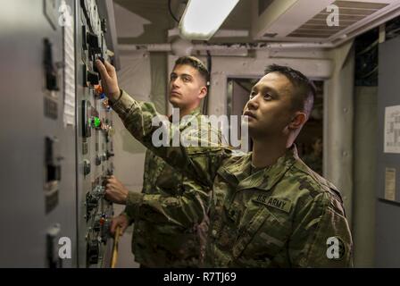 Spc. Huy Dinh and Spc. Dylan Nice, U.S. Army Reserve watercraft operator and engineer Soldiers from the 949th Transportation Company, a unit which specializes in watercraft operations, cargo and watercraft engineering, pose in the engine control room of a Logistics Support Vessel in Baltimore, Md., on April 7-8, 2017. Stock Photo