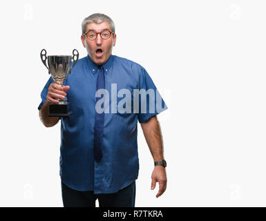 Handsome senior successful man holding trophy over isolated background scared in shock with a surprise face, afraid and excited with fear expression Stock Photo