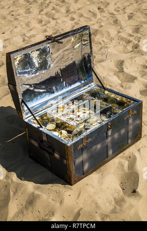 Treasure chest with gold and silver coins on the sand Stock Photo