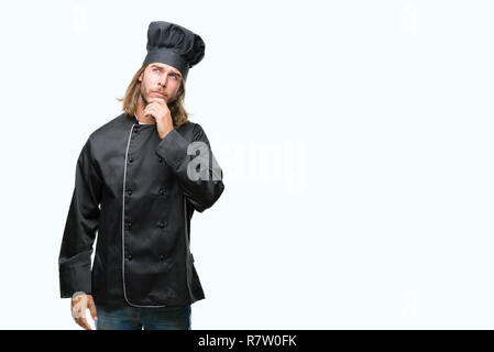 Young handsome cook man with long hair over isolated background with hand on chin thinking about question, pensive expression. Smiling with thoughtful Stock Photo