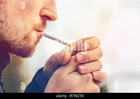 Man with stubble lights a homemade cigarette and smokes. Bad habit concept Stock Photo