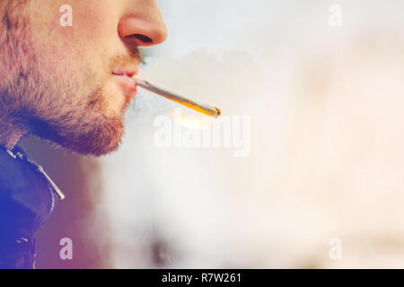Man with stubble lights a homemade cigarette and smokes. Bad habit concept Stock Photo