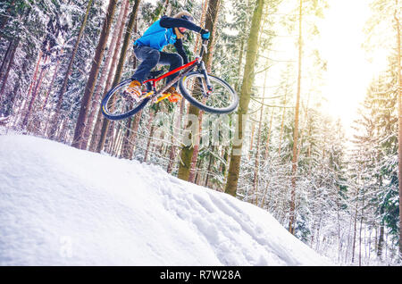 Silhouette of a cyclist in a jump. Mountain biking on trails in a snowy forest. Extreme winter sport. Bike rider flies through the air Stock Photo