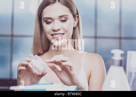 Pleasant young woman looking into a jar of face cream Stock Photo