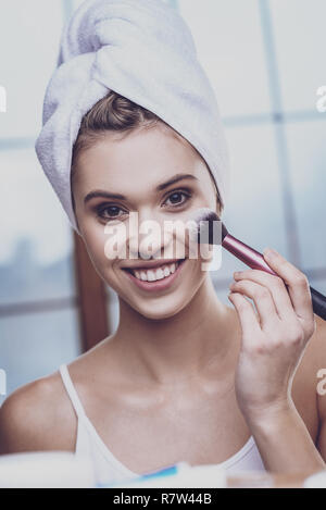 Young woman applying blush on her cheeks Stock Photo