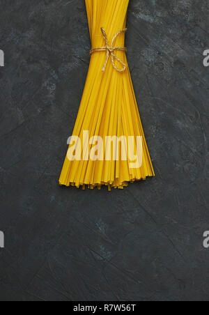 Uncooked pasta tied with a rope on concrete against black background. copy space. view from above. Stock Photo