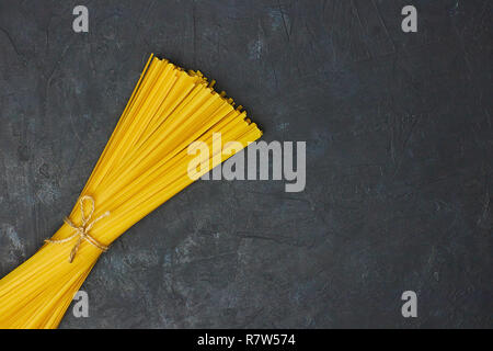 Uncooked pasta tied with a rope on concrete against black background. copy space. view from above. Stock Photo