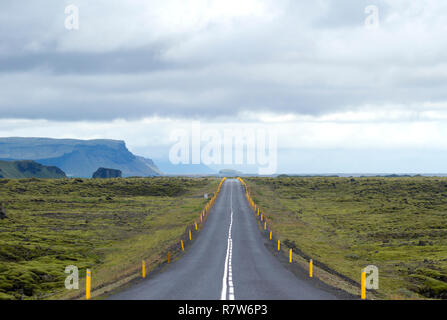 ring road route around iceland crossing an ancient lava river covered by moss with the cliffs and the sea in the background Stock Photo