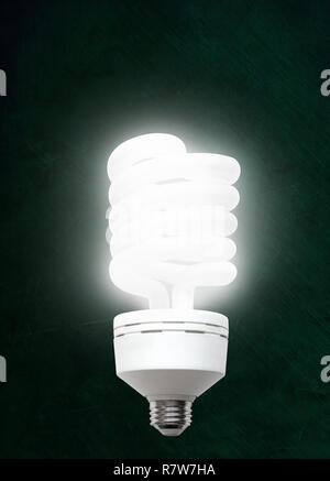 Illuminated CFL compact fluorescent light bulb against chalkboard background with copy space. Stock Photo