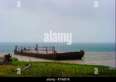 An abandoned barge sits along the banks of the Columbia River.  Steady rain falls on the already rusty, decaying deck as the stormy weather provides Stock Photo