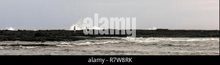 Honaunau, Hawaii - Waves break behind a man and a woman walking on rocks that extend into the Pacific Ocean on Hawaii's Big Island. Stock Photo