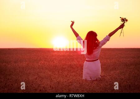 young girl joys on the wheat field at the sunset time Stock Photo