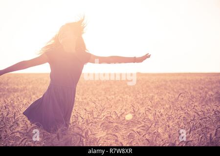 young girl joys on the wheat field at the sunset time Stock Photo