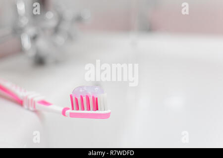 Pink toothbrush with toothpaste on the background of the washbasin. Small depth of field. Stock Photo