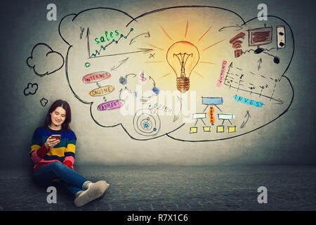 Attractive young woman sitting on the floor using mobile phone, positive thinking concept, modern technology network and idea concept. Lightbulb sketc Stock Photo