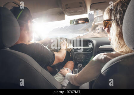 Happy couple driving in a car with the sun shining through the window Stock Photo