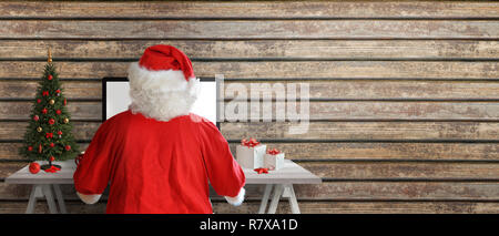 Santa Claus send greeting cards online. Copy space beside on wooden wall. Stock Photo