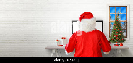 Santa work on a computer in his room. White brick wall in background with a free text space. Stock Photo
