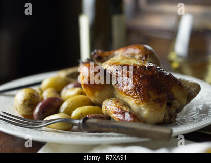 A baked Cornish hen on a plate with a fork, potatoes and white wine. Stock Photo