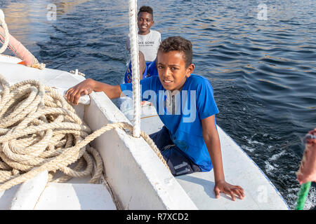 Aswan, Egypt - September 13, 2018: Egyptian children in a surf table hold on to the side of tourist boat in Nile river waiting for a tip Stock Photo