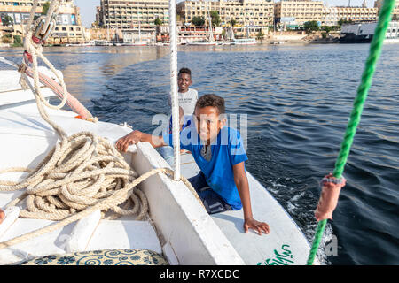 Aswan, Egypt - September 13, 2018: Egyptian children in a surf table hold on to the side of tourist boat in Nile river waiting for a tip Stock Photo