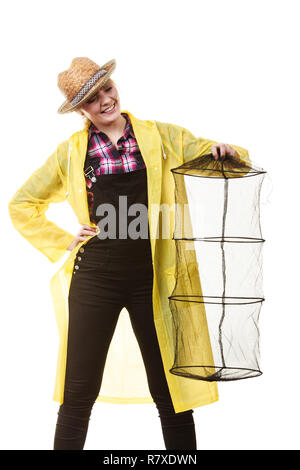 Spinning, angling, cheerful fisherwoman concept. Happy woman in yellow raincoat holding empty fishing keepnet, having fun. Stock Photo