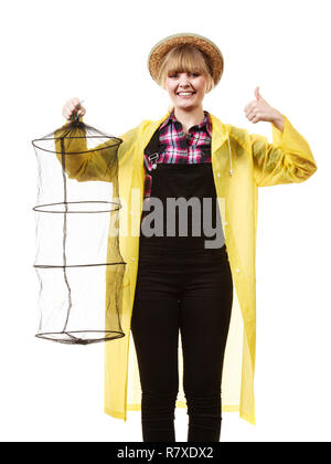 Spinning, angling, cheerful fisherwoman concept. Happy woman in yellow raincoat holding empty fishing keepnet, having fun. Stock Photo