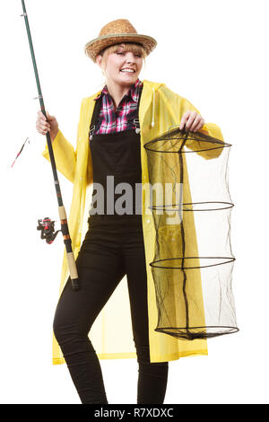 Spinning, angling, cheerful fisherwoman concept. Happy woman in yellow raincoat holding fishing rod and keepnet having fun. Stock Photo