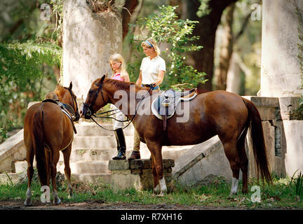 Teenage girl standing with her mid-adult mother and two horses. Stock Photo