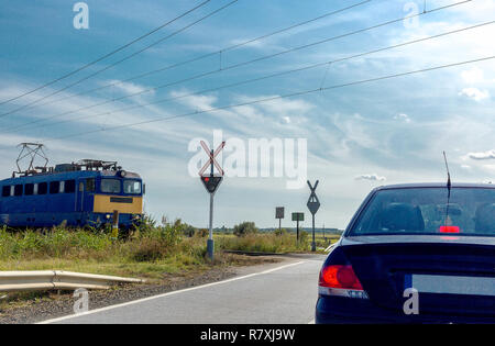 The electric train approaching railroad crossing. Car standing in front of the railway crossing with traffic light and road sign without a barrier Stock Photo