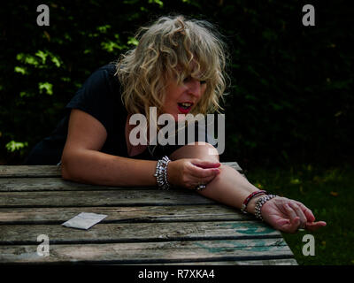 A woman injecting drug into her arm with a syringe in the street and a dose of drug to the side Stock Photo