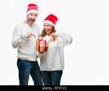 Middle age hispanic couple wearing christmas hat and holding gift over isolated background very happy pointing with hand and finger Stock Photo