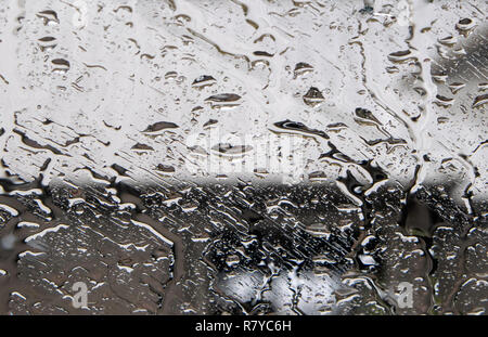 Raindrops and rivulets gather on the windshield of a vehicle, seen from inside. Stock Photo