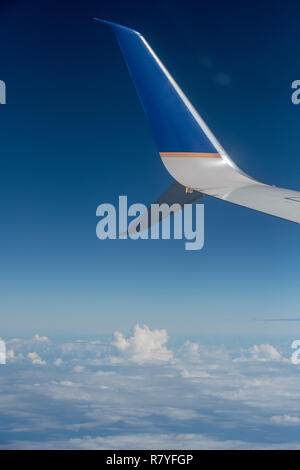Plane wing from a plane window with cumulus clouds and blue sky in background - plane travel - airplane flight Stock Photo