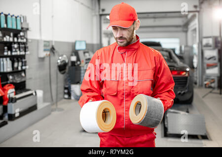 Auto mechanic in red uniform holding new and used air filter standing at the car service Stock Photo